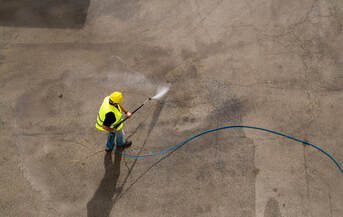 An above picture shot of a man in a hard hat washing away at the ground using a pressure washer.