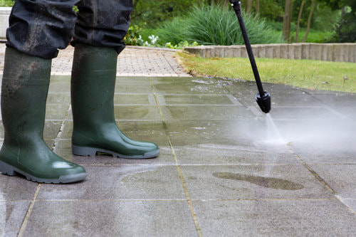 A worker in green boots spraying the floor using a pressure washer.