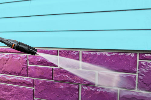 A pressure washer being sprayed on purple bricks.