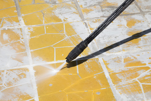 A pressure washer being used to clean off a cracked yellow surface.