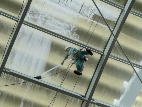 A worker standing on a glass ceiling as he tries to clean it.