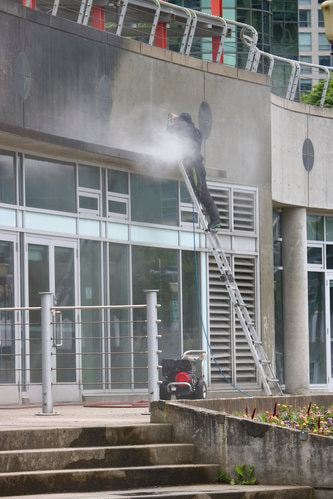 A male worker cleaning a commercial building using a ladder.