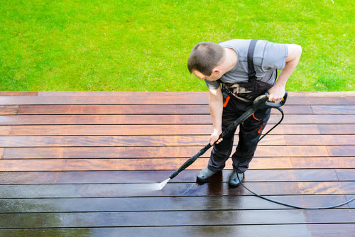 A worker cleaning a pressure washing a dirty wooded deck.