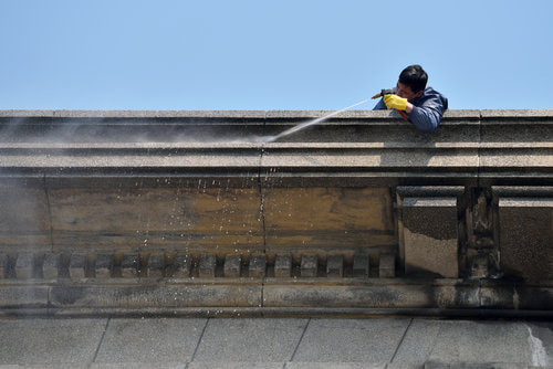 A worker spraying down  a building with a hose from the roof.