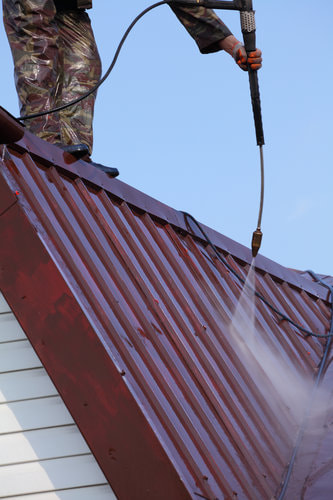 A picture of a residential roof being cleaned by a pressure washer.